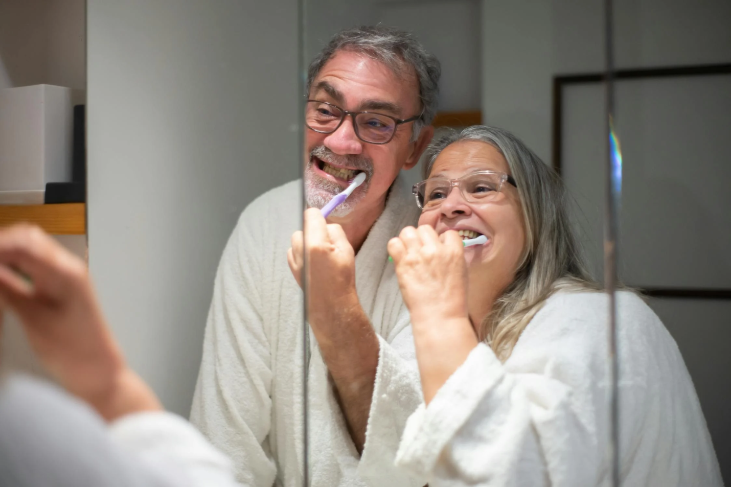 An older couple brushes their teeth.