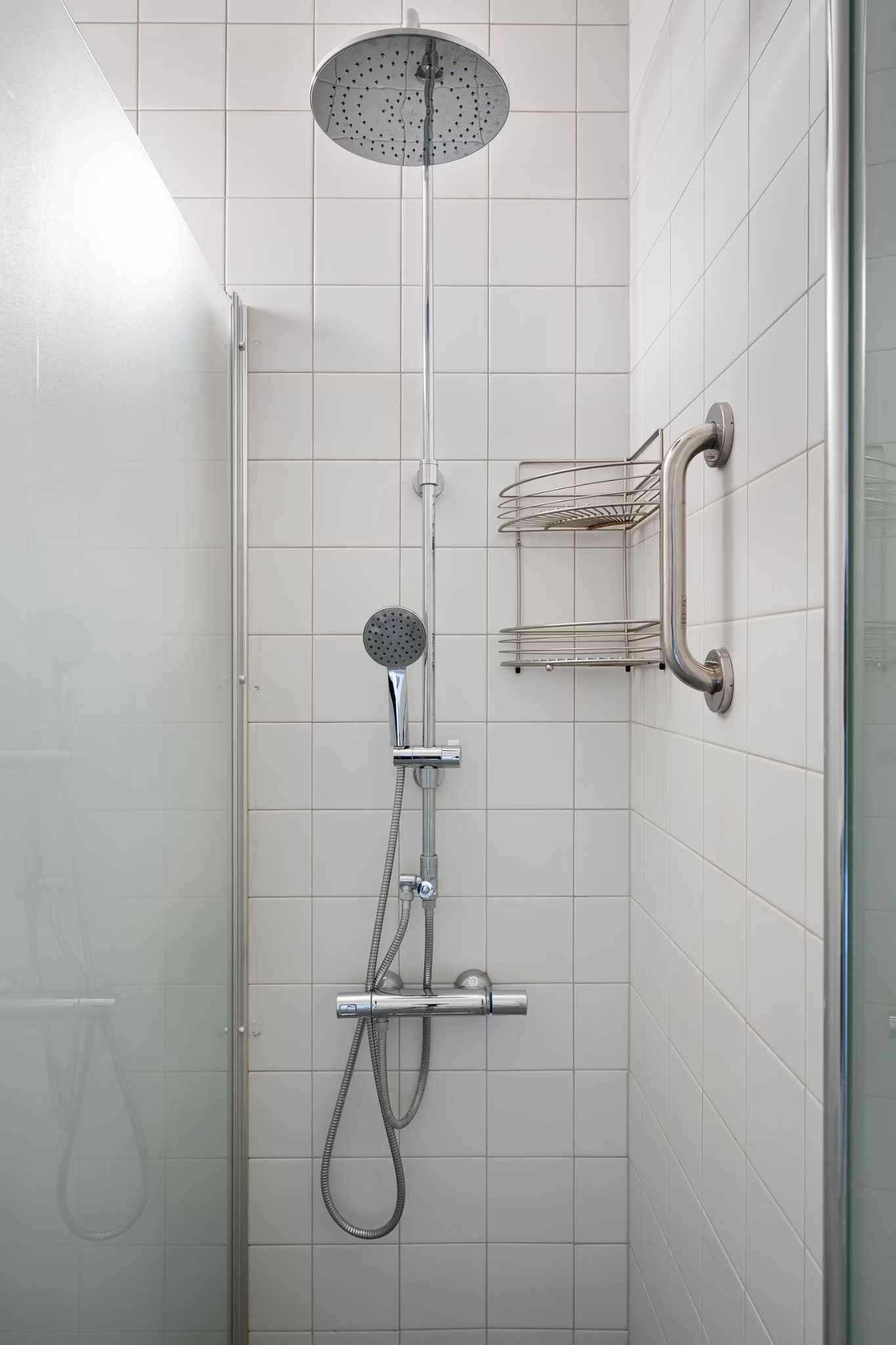 a walk-in shower with glass door and shelf on the wall inside