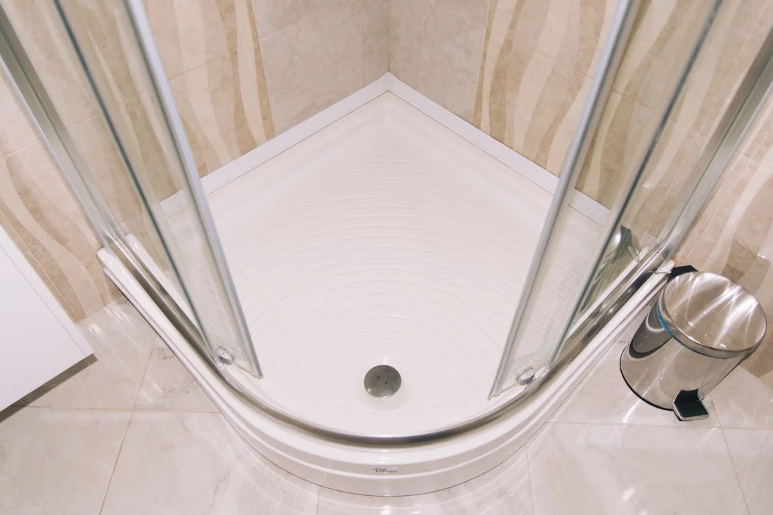 close up of a walk in showers white floor with a drain and glass doors